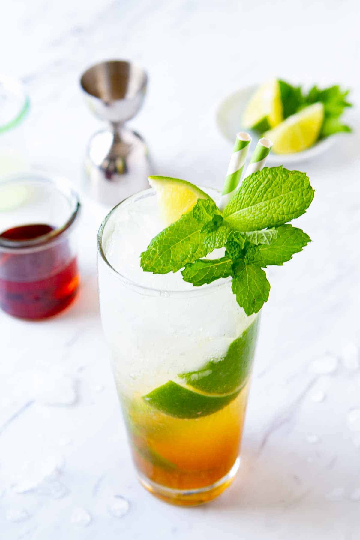 glass of dark rum mojito with ingredients in the background