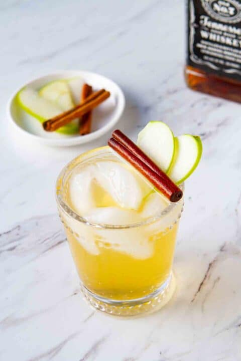 Glass with apple slice  and cinnamon stick garnish.